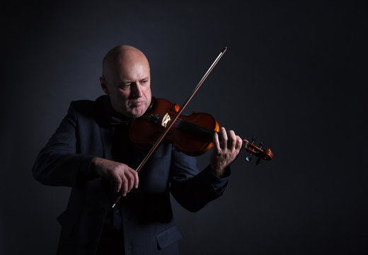 A man passionately playing the violin on dark background.