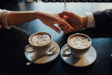 hand girl in a man's  at the table with cups of coffee in the foreground