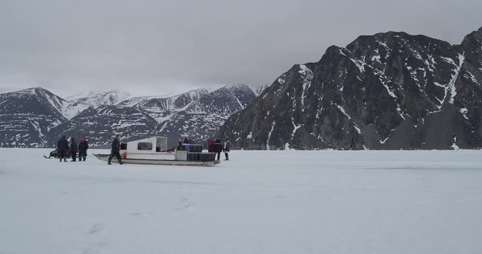 Tourists next to skidoos and trailers on sea ice near mountains