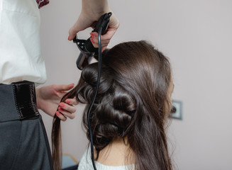 Fototapeta premium Hairdresser curling woman hair with electric iron curler tong. Hairstylist making woman hairstyle.