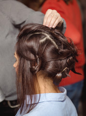 Naklejka premium Hairdresser curling woman hair with electric iron curler tong. Hairstylist making woman hairstyle.