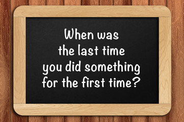 Inspirational motivating quote on chalkboard with wooden background. When was the last time you did something for the first time?