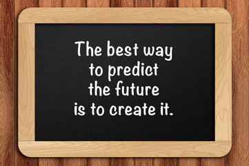 Inspirational motivating quote on chalkboard with wooden background. The best way to predict the future is to create it.