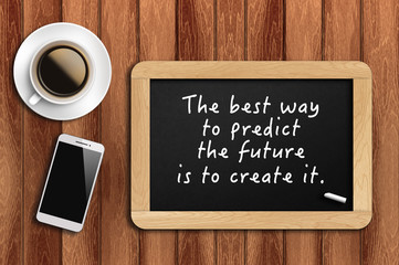 Inspirational motivating quote on chalkboard with coffee, phone and wooden background. The best way to predict the future is to create it.
