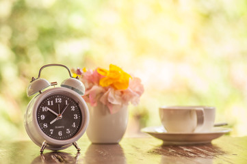 Start up concept, Alarm clock with coffee cup and fresh flowers on wooden table with natural background