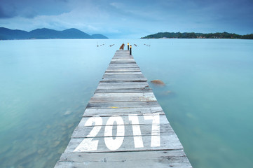 long exposure of wooden jetty and number 2017 at sea facing island with cloud and sky at twilight.