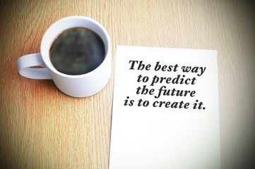 Inspirational motivating quote on paper with black coffee on the table. The best way to predict the future is to create it.