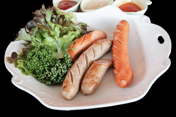 Grilled sausages and vegetables on black background