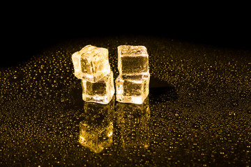Ice cubes in yellow light on black wet table.