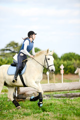beautiful young woman riding horse and training for jump hurdle equitation competition outdoor