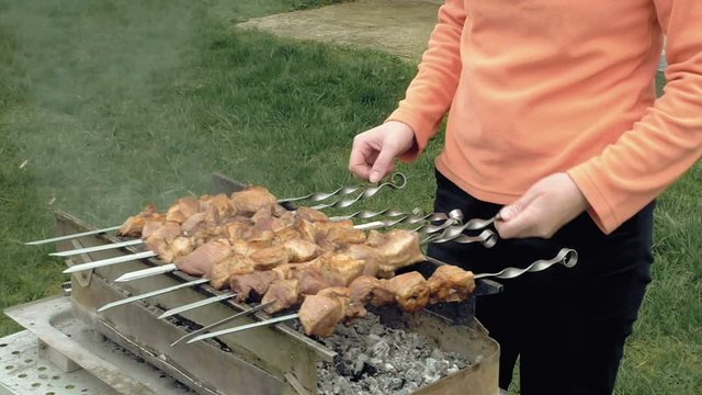 Girl cooks barbeque skewers with meat on hot coal ember brazier Outdoors picnic concept.