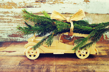 Children's wooden car is lucky fir-tree branches against the background of an old vintage board. Wooden car carrying a christmas tree. Christmas or New Year's background