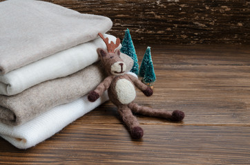 Stack of knitted clothes in nude beige tones. Cashmere sweaters, wool cardigan, felt elk and little Christmas tree on a wooden background. Concept of Winter time and Christmas holiday. Copy space.