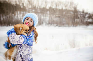 smiling woman holding her pet dog in his hands near face, hugging. Spitz breed dog playing with a woman walking outdoors winter day, warm clothing. love and care for the pet, dog walking