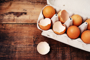 Chicken eggs and shells of broken eggs in a cardboard tray on a wooden table surface. Eggs