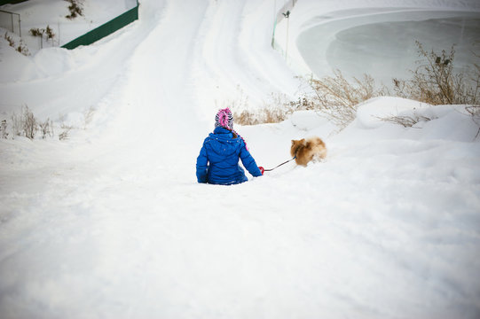 girl rolls from the hill in the snow with a dog