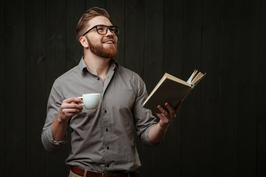 Man Looking Up While Holding Open Book And Cup