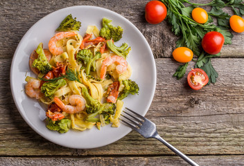 Pasta linguine with shrimps and broccoli in plate on wooden background.