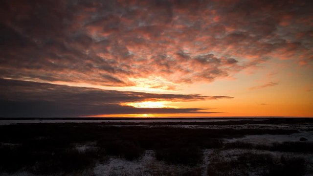 Timelapse sun setting behind clouds in orange tundra