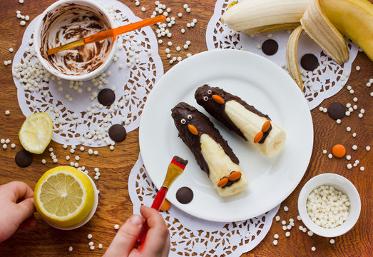 Kid hands preparing creative breakfast from banana in chocolate