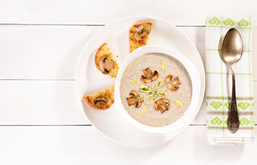 Soup with champignons, leek and crispy croutons on white background, top view.