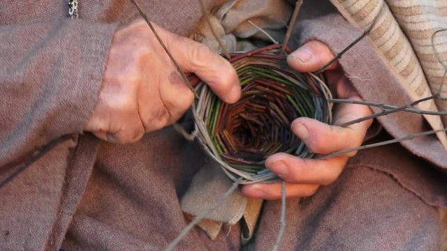 elderly man is weaving a basket with gorse