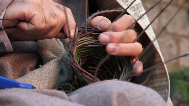elderly man is weaving a basket with gorse