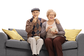 Joyful mature couple sitting on a sofa and eating popcorn