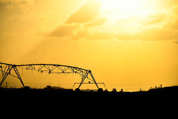 Pivot overhead irrigation in silhouette with sunset background.