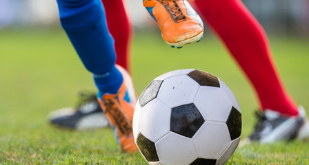 Foot kicking soccer ball on the green field