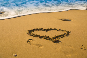 Drawing a heart on the beach sand on the beach with sea waves in the background. Selective focus. Beautiful deserted beach. Trace of human foot on the sand.