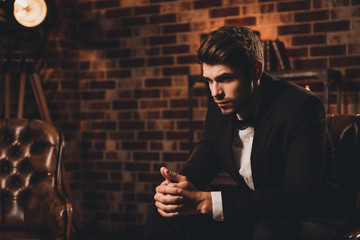 Young minded businessman in black suit sitting on leather sofa