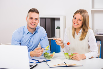 Businesswoman and businessman sitting in office and having lunch break.
