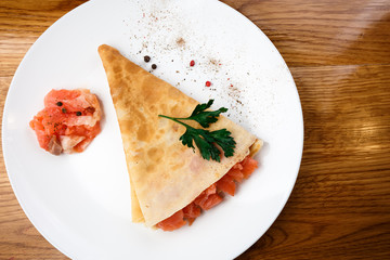 pancake with red fish on a white plate. wooden table.