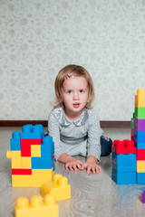 Child girl lying near bright plastic construction blocks. Toddler playing on the floor. Developing toys. Early learning.