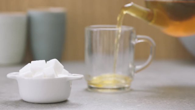 Pouring hot tea from teapot and putting sugar cubes in the teacup. 
