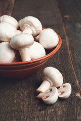 Fresh white mushrooms champignon in brown bowl on wooden background. Close up.