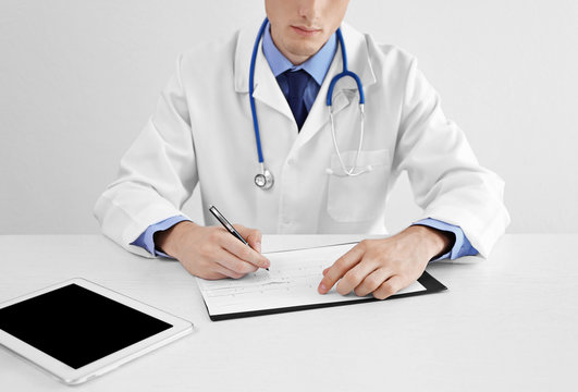 Male doctor making notes on cardiogram while sitting at table