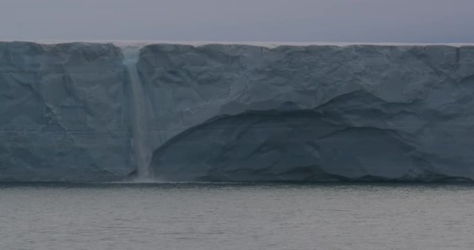 Medium Waterfall Flowing Into Ocean Over Edge Of Glacier