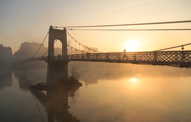 Obraz premium Pedesrtians on the monumental Passerelle du College bridge over the Rhone river in Lyon on a foggy morning.