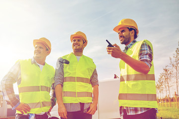 happy male builders in vests with walkie talkie