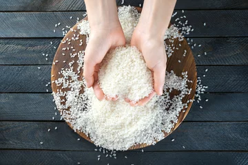 Rolgordijnen Female hands full of white rice on wooden background © Africa Studio