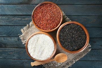 Different types of rice in bowls on wooden table, top view