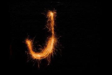 Letter J made of sparklers on black