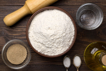 Ingredients for homemade pizza dough on dark rustic background.
