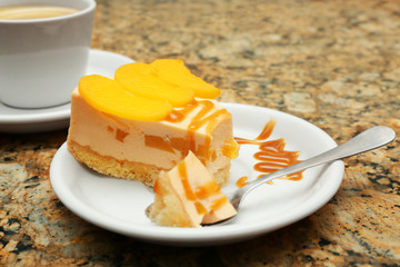 Plate with tasty peach cheesecake and spoon on table, close up view
