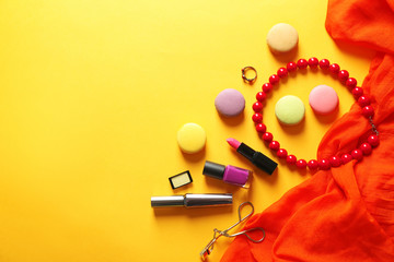 Makeup products, accessories and macaroons on yellow background