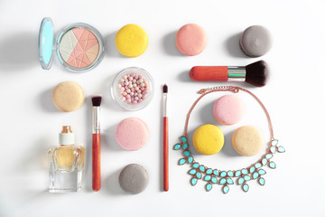Makeup products and macaroons on white background