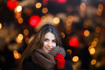 Girl with long hair on European Christmas Market. Young woman Enjoying Winter Holiday Season. Blurred  Lights  background, dusk. Selective focus