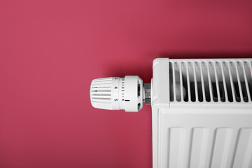Heating radiator with temperature regulator on pink background, closeup